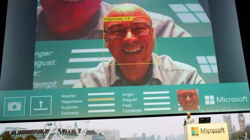 Large screen at Microsoft conference showing close up of mans smiling face with AI tool correctly categorising as 'happy' face