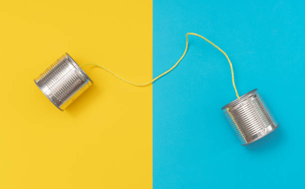 Communication device of two tins connected by string against bright blue and yellow background