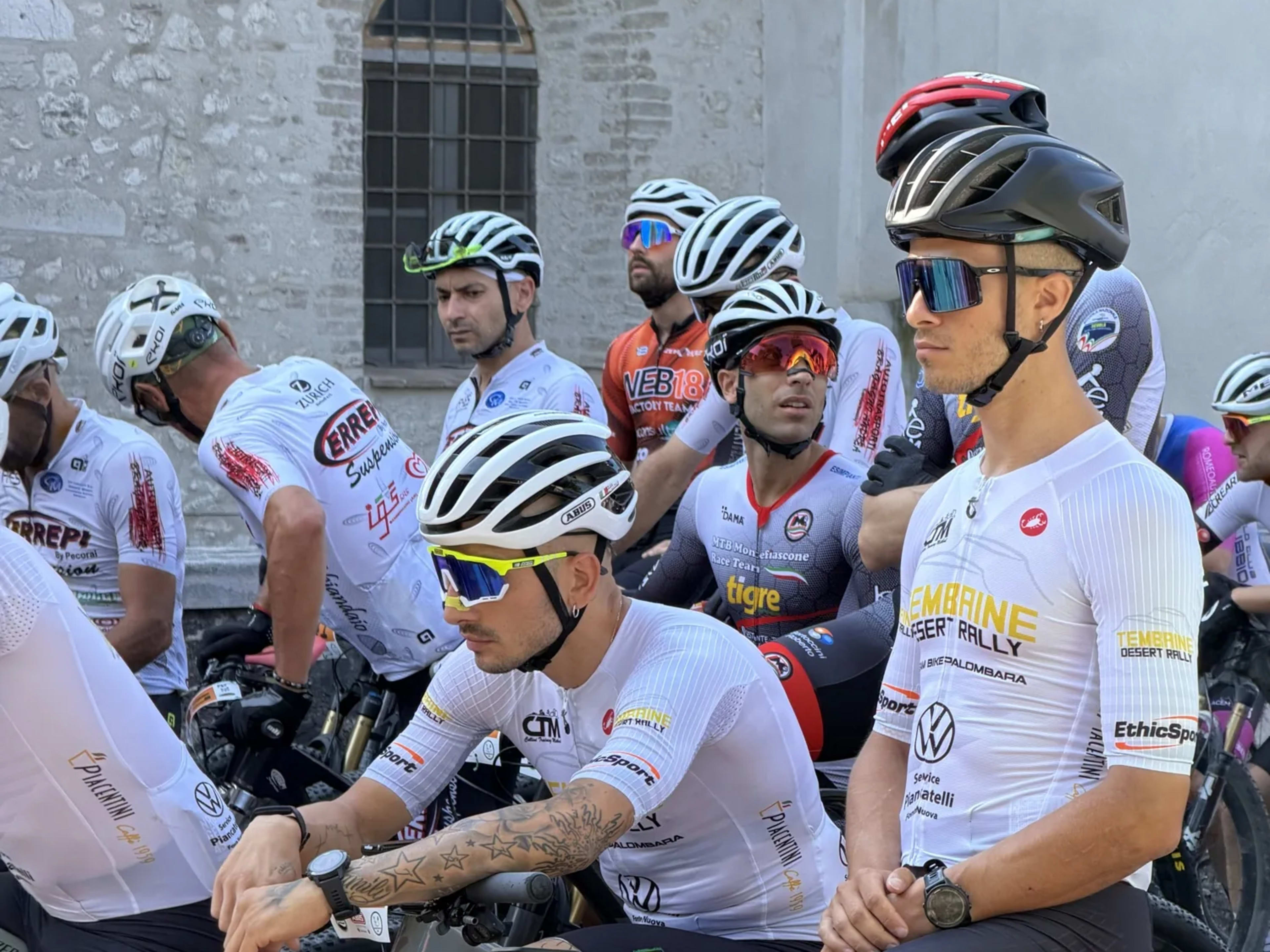 Concorrenti in maglia bianca attendono in griglia davanti alle mura antiche