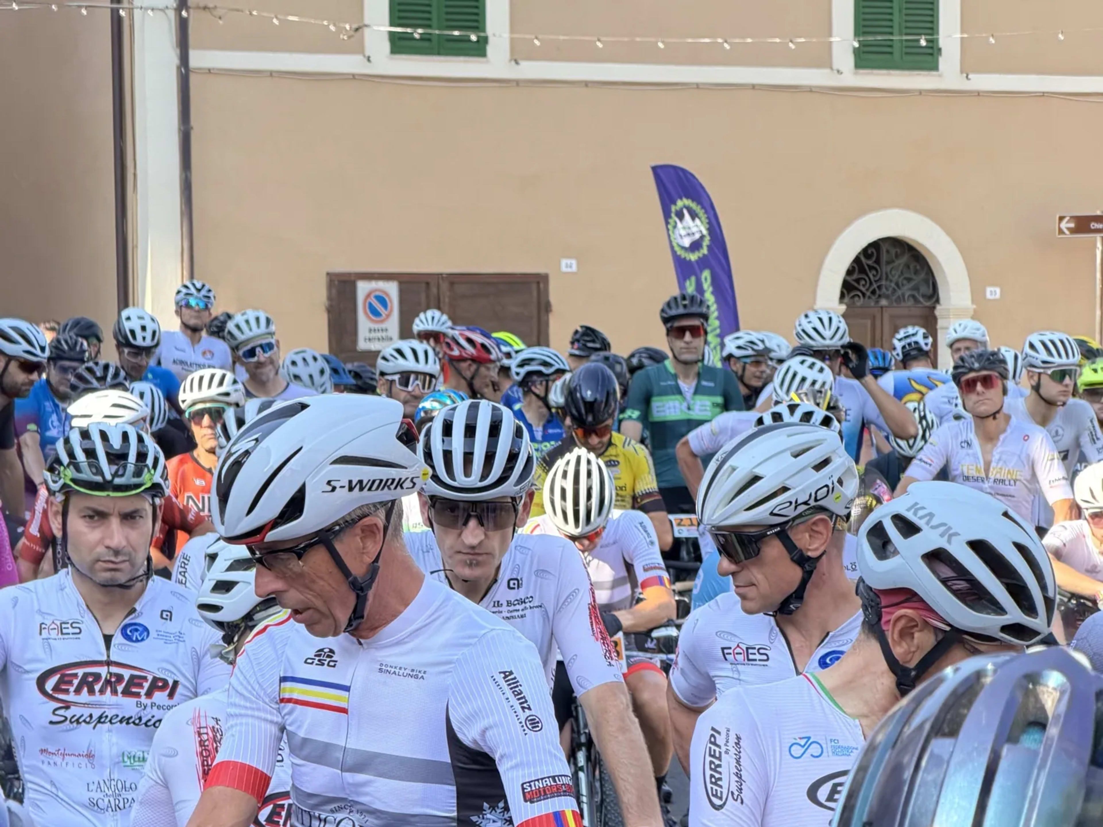 Bikers con pettorale 42 schierati davanti agli edifici del borgo