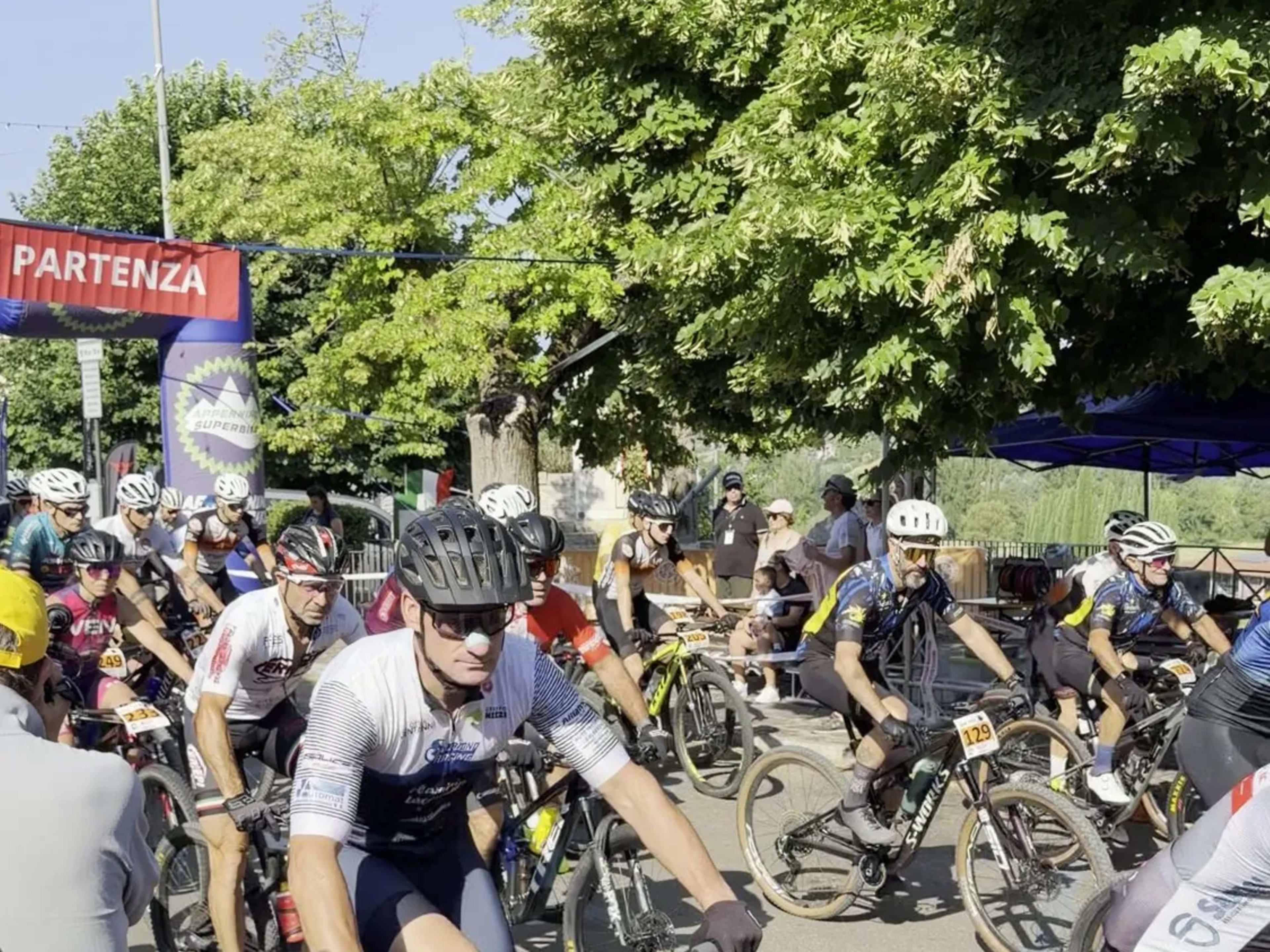 Concorrenti pedalano sotto lo striscione Partenza nelle prime fasi di gara