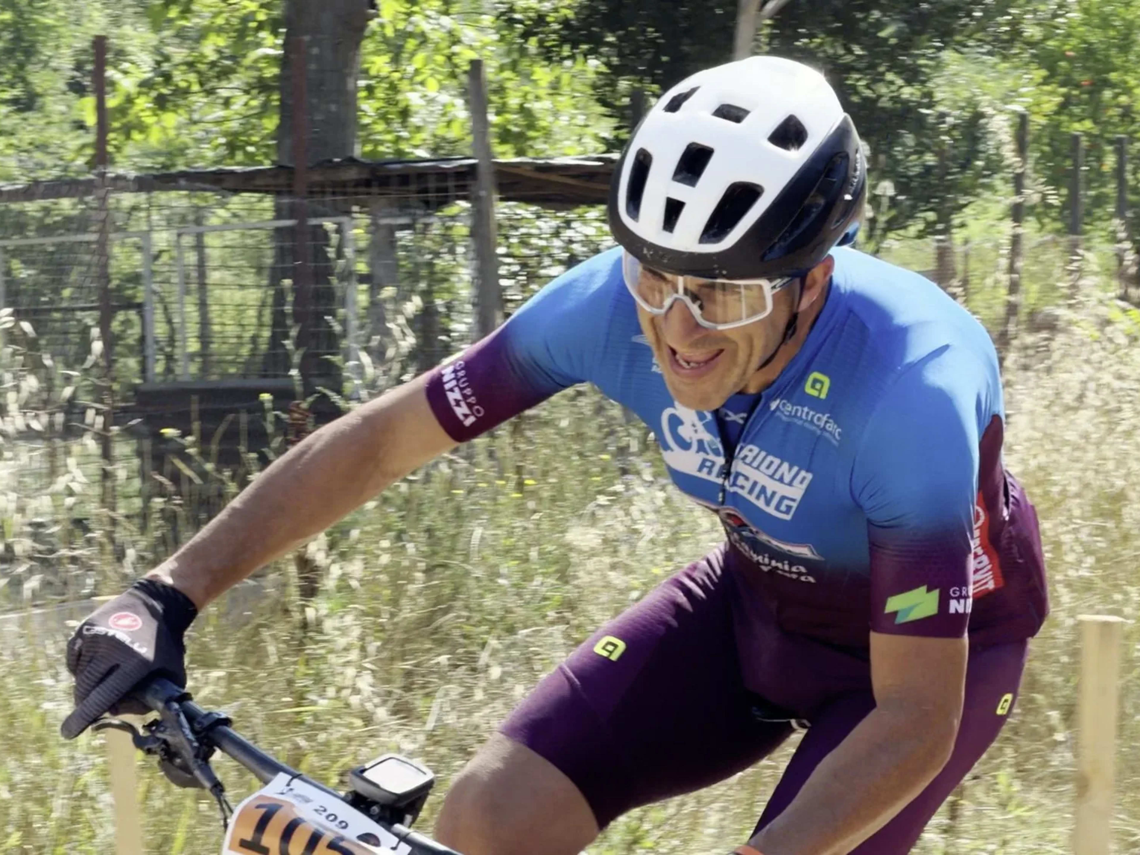 Ciclista in maglia azzurra spinge sui pedali tra l'erba alta del percorso