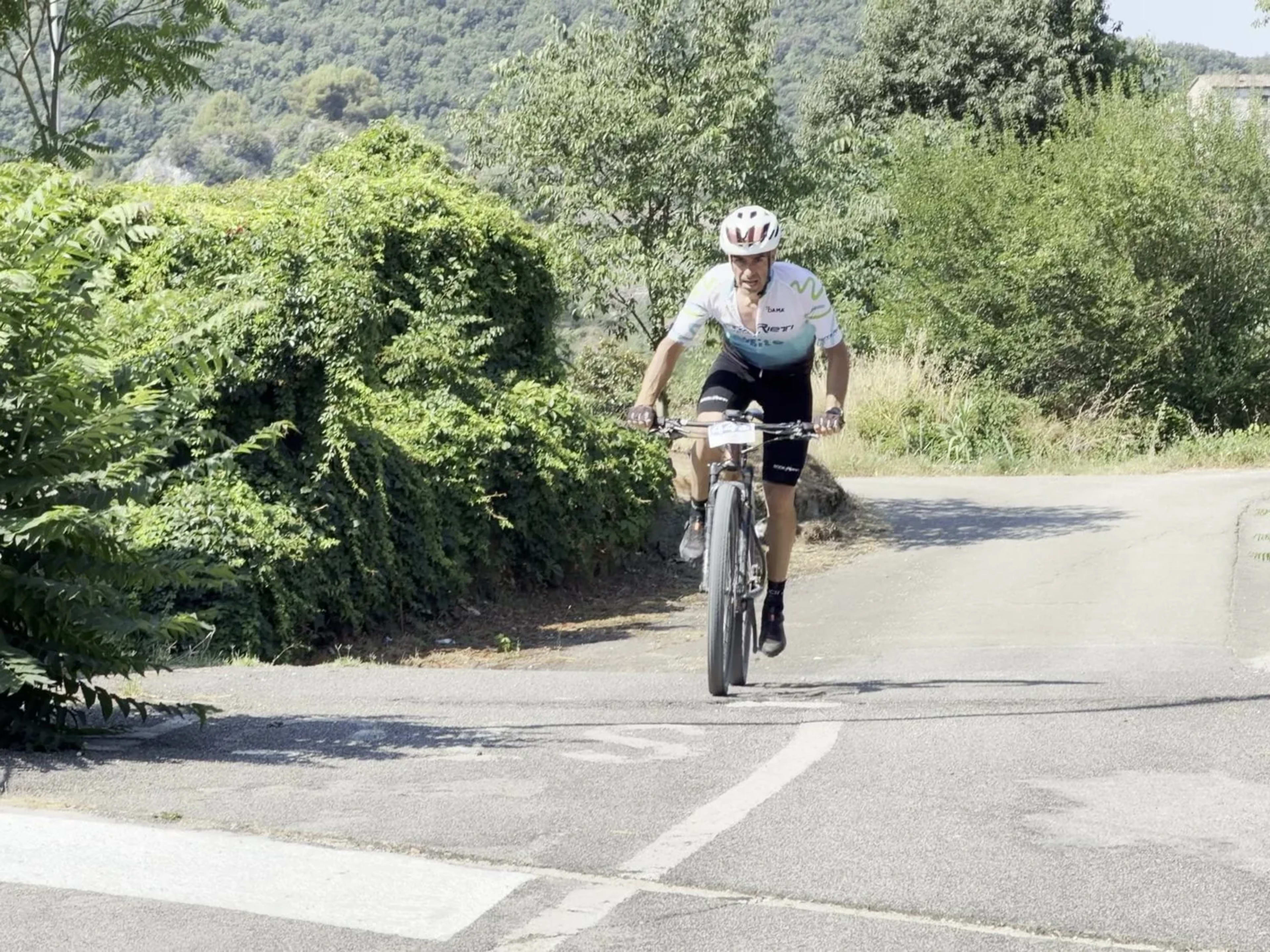 Biker in salita su strada asfaltata immersa nella vegetazione