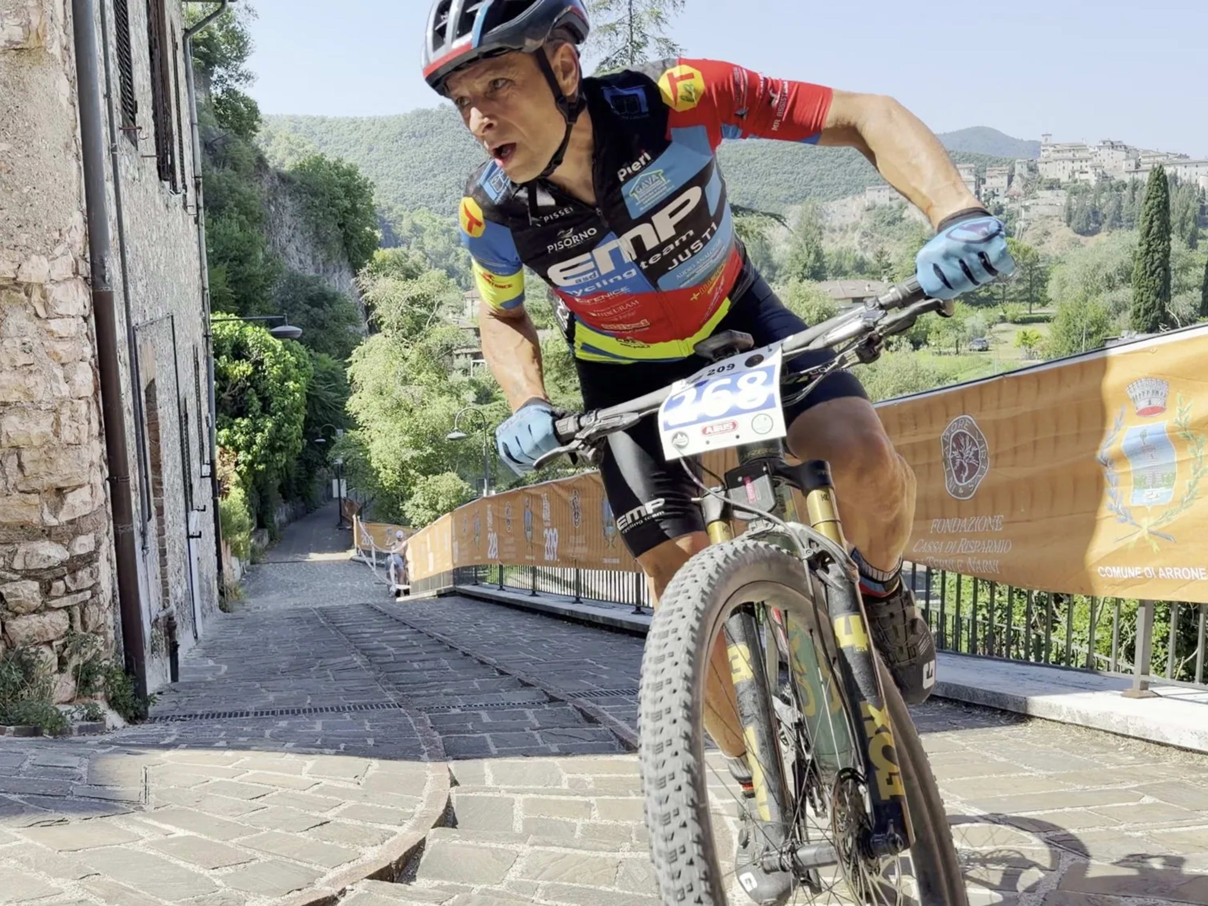 Biker affaticato in salita sull'acciottolato del paese di Arrone