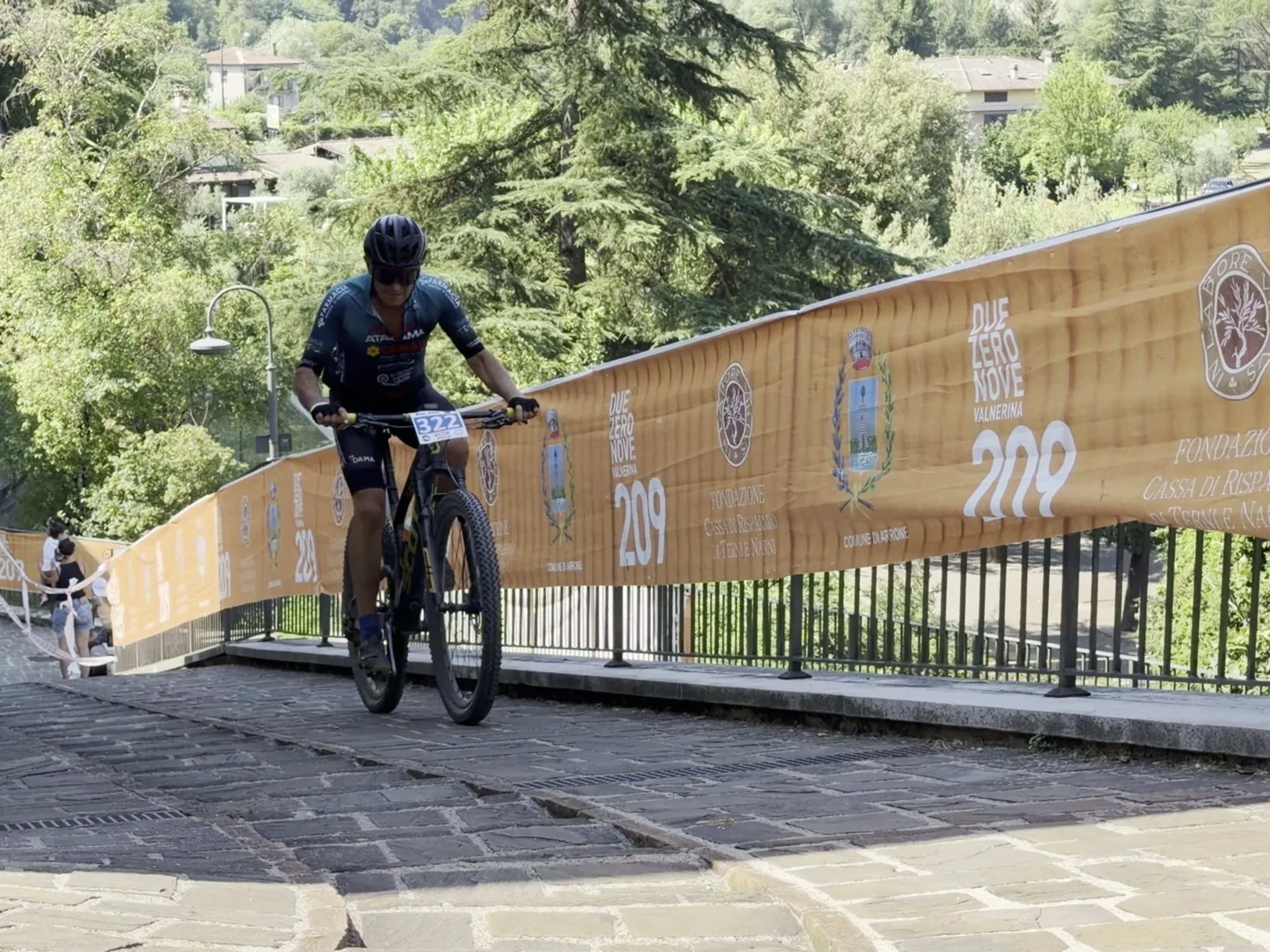 Biker pedala lungo le transenne con i loghi della gara e il panorama