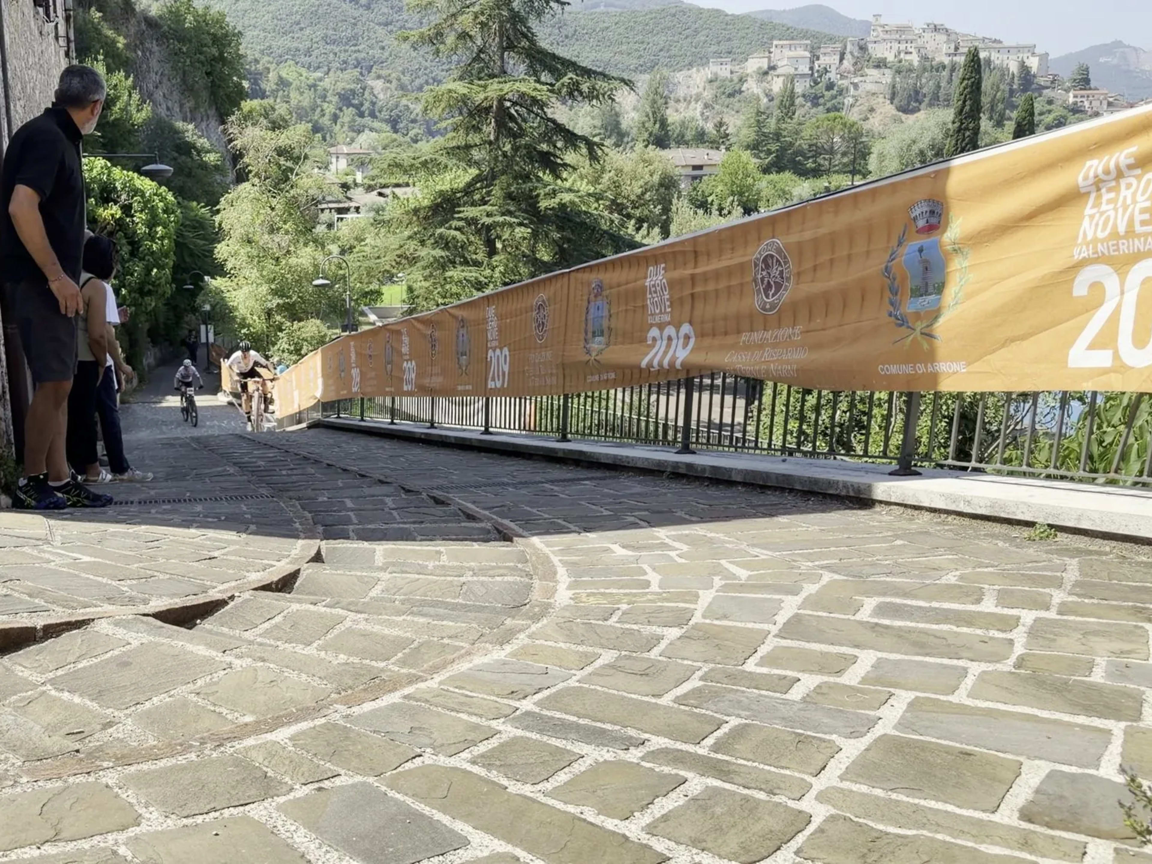 Vicolo lastricato del borgo di Arrone con le barriere gialle del percorso e le colline della Valnerina