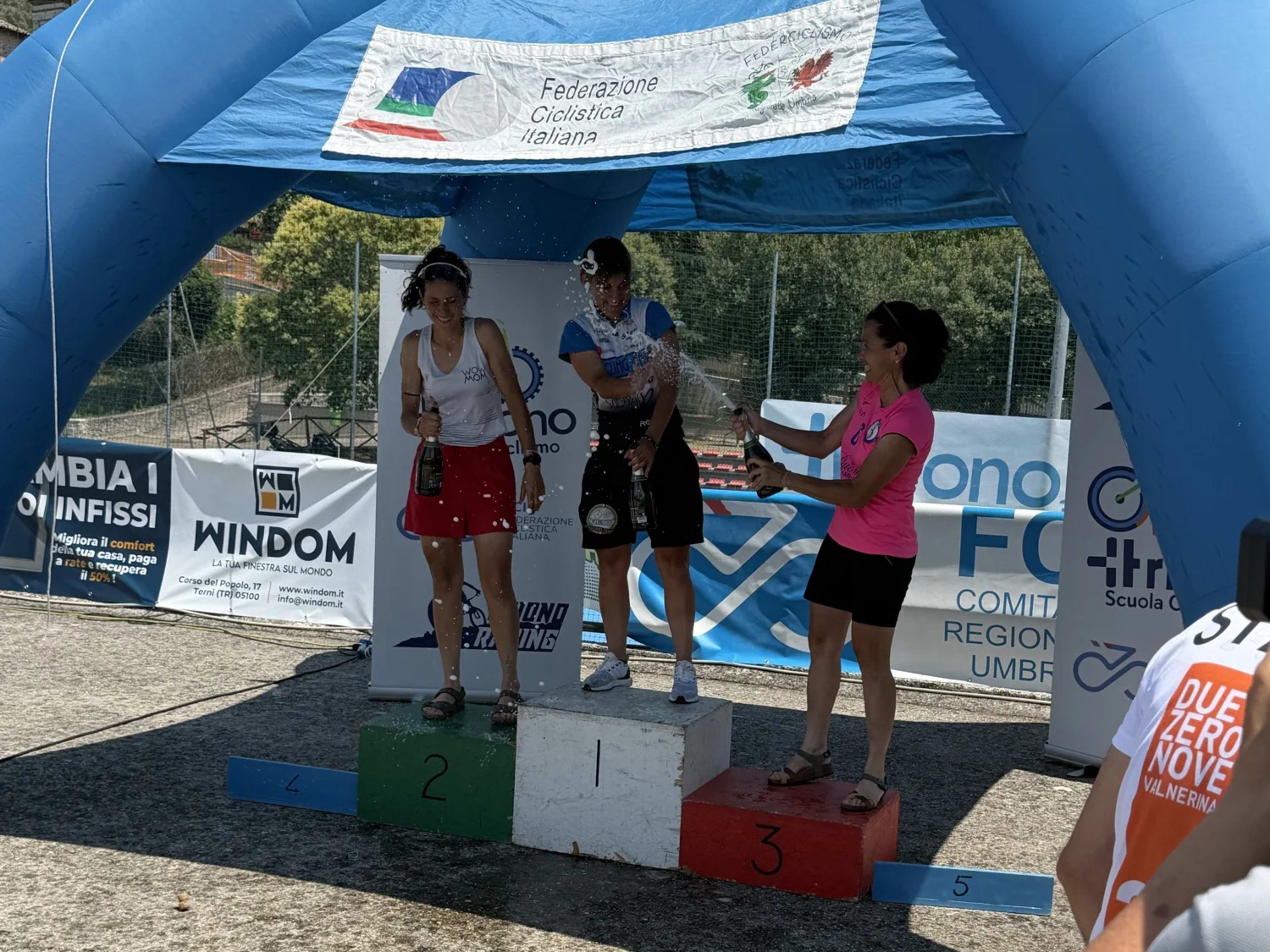 Premiazione femminile sul podio con i premi e lo spumante in mano