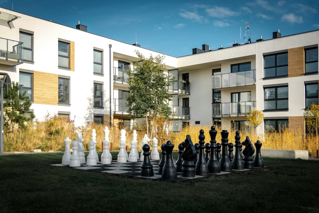 Giant chess set in a courtyard with modern buildings.