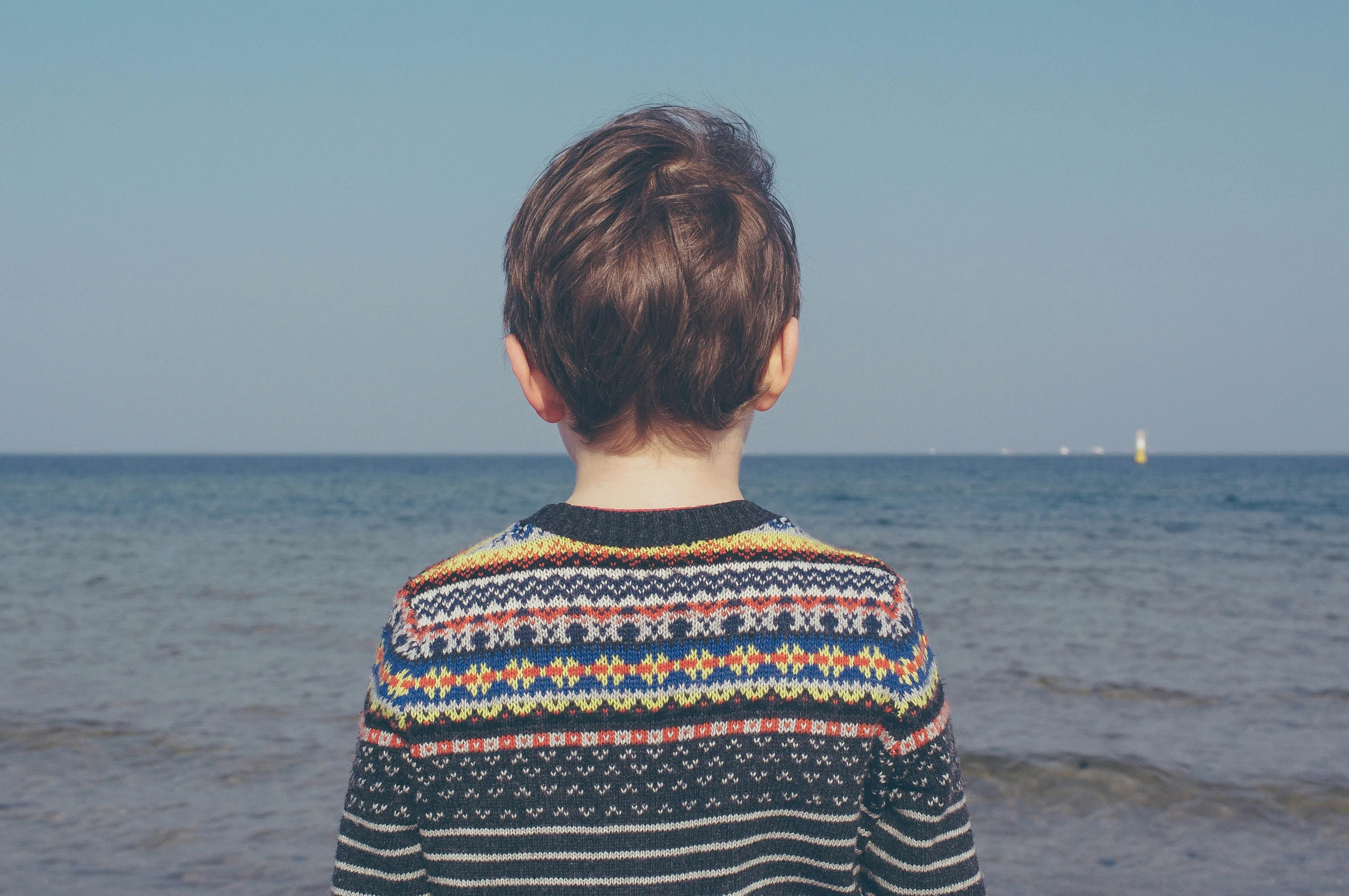 Child wearing a sweater standing with the sea in the background.
