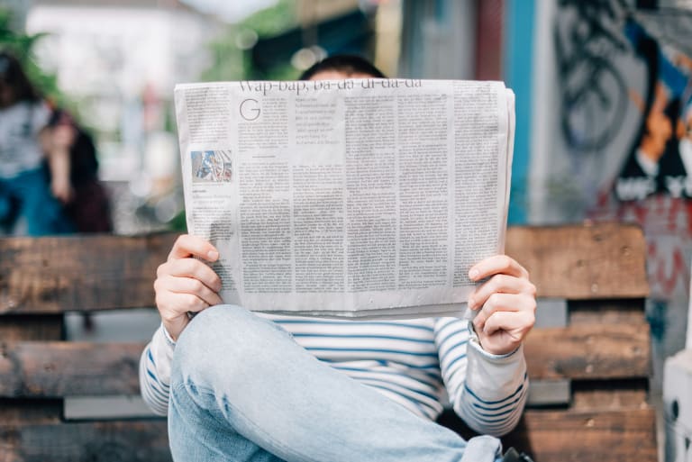 Man sitting on bench reading newspaper.