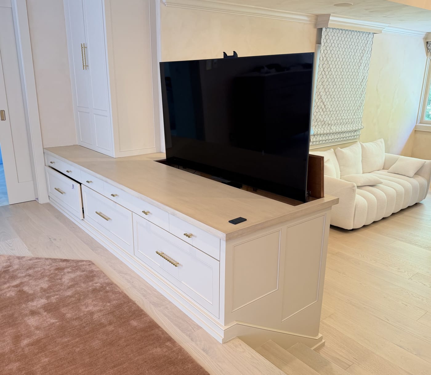 Television raised on a motorized lift from white custom cabinetry