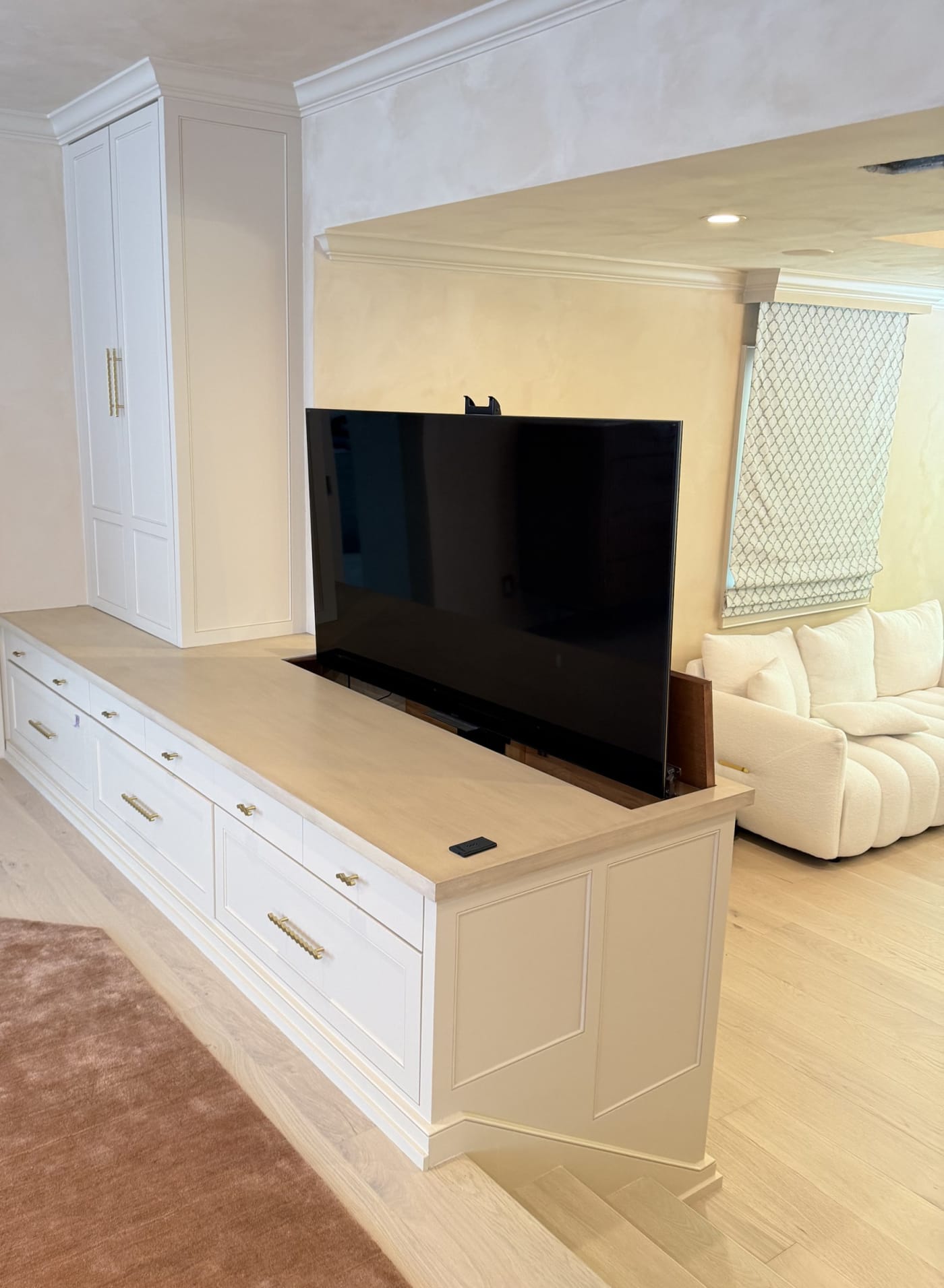 Television raised on a motorized lift from white custom cabinetry