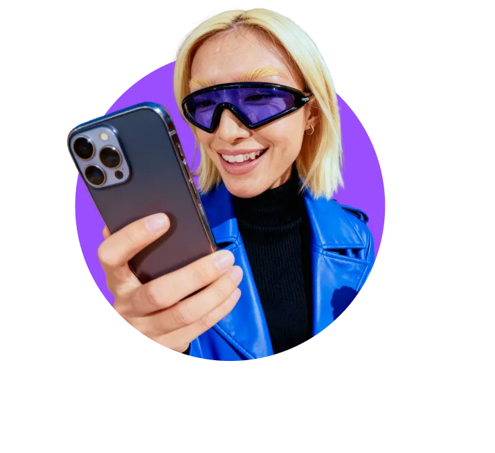 Person in a blue jacket and tinted visor-style sunglasses smiling while looking at their phone against a light circular background.