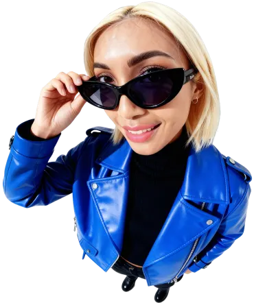 A confident person wearing a bright blue leather jacket and black cat-eye sunglasses smiles at the camera in a studio with a white curved backdrop.