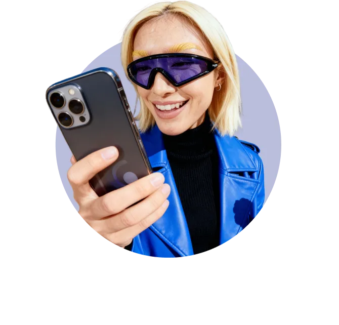 Person in a blue jacket and tinted visor-style sunglasses smiling while looking at their phone against a light circular background.