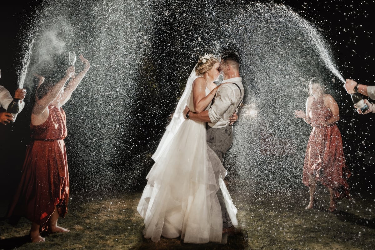 Bride and groom celebrating with champagne spray at night with bridal party