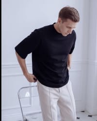 365.APParel Oversize T-shirt Black — man, standing by chair, looking down, full body, indoor editorial