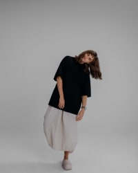 365.APParel Oversize T-shirt Black — woman, full body front, tilting sideways, hair falling, beige bubble skirt, studio