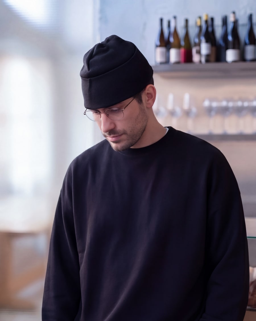 365.APParel Oversize Sweatshirt Black — man, cropped front view, looking down, glasses, beanie, wine bar, indoor
