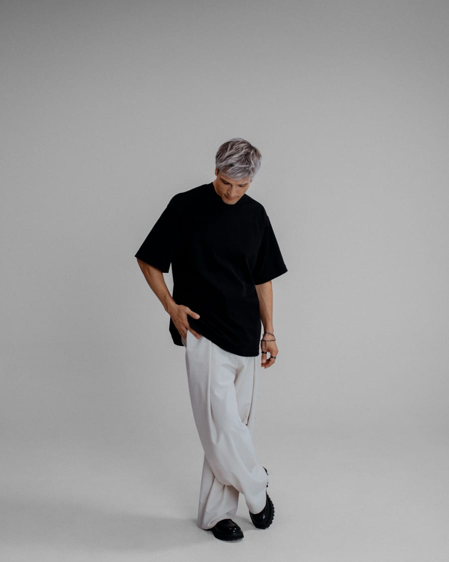 365.APParel Oversize T-shirt Black — man, full body front, gray hair, looking down, white trousers, studio