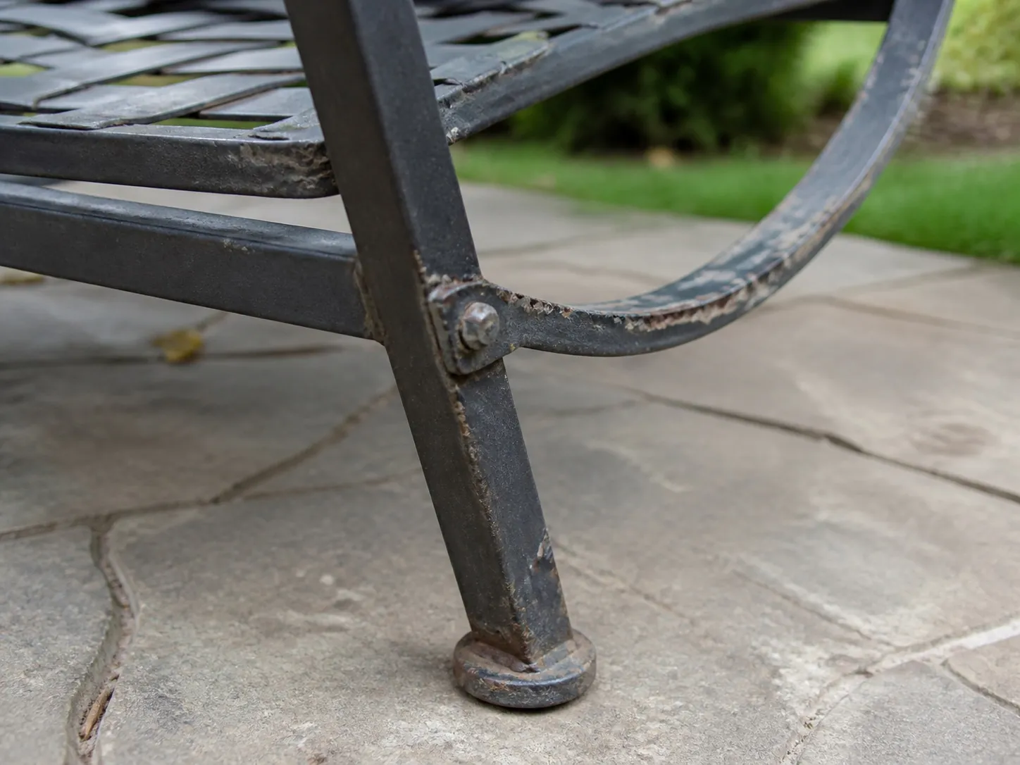 Close-up of peeling coating and visible rust around a metal patio chair joint and foot