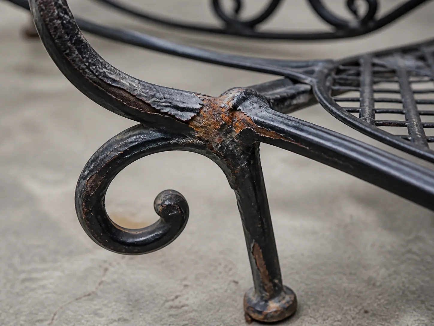 Close-up of peeling black coating and surface rust at a wrought iron furniture joint