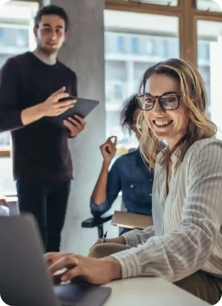 Smiling woman with glasses working on a laptop with colleagues, representing expert guidance and support