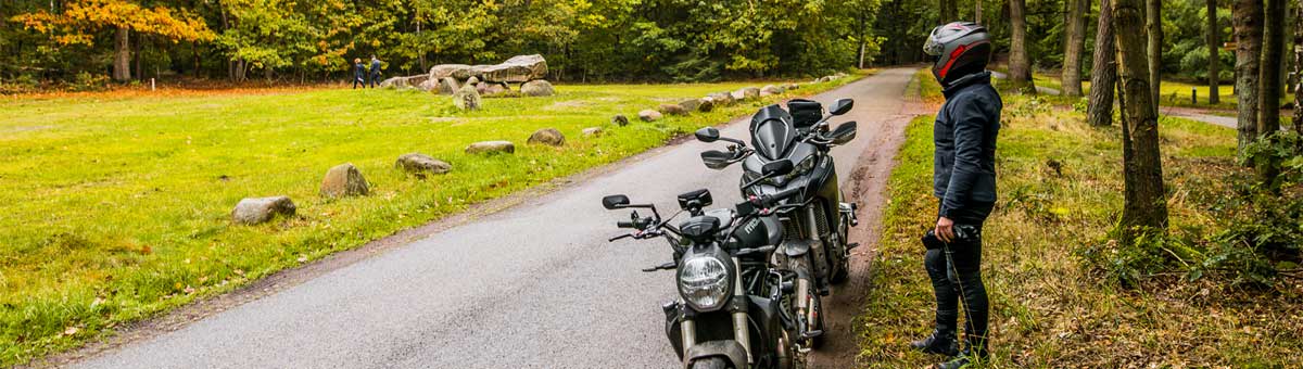 Motorrijder naast 2 motoren aan de rand van een bos
