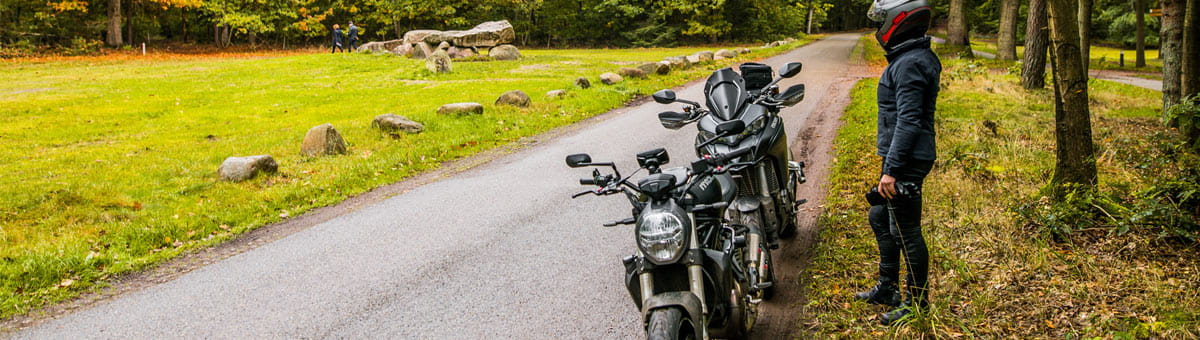 Motorrijder staat naast 2 motoren in de berm