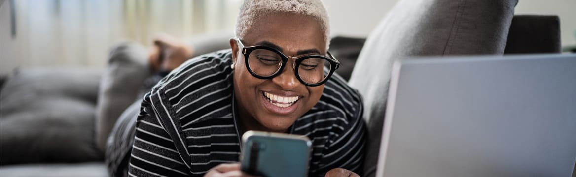 vrouw ligt op de bank met mobiel en laptop