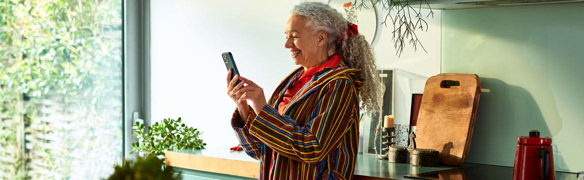 oudere vrouw staat met telefoon in de keuken