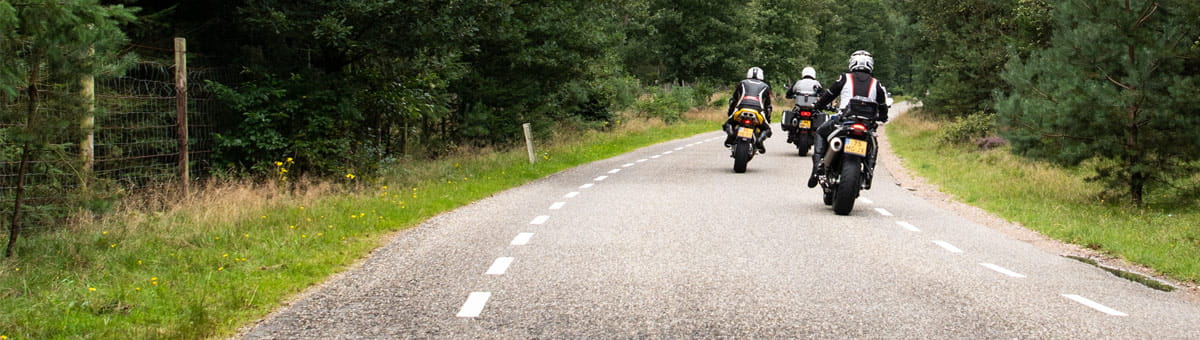 Drie motorrijders rijden over een bosweg