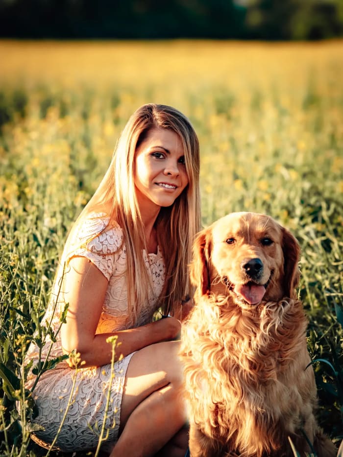 Nő guggol golden retrieverével a virágos mezőn