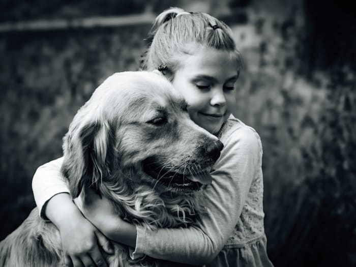 Fekete-fehér kép: kislány átöleli golden retrieverét