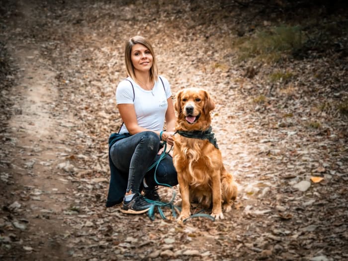Fiatal nő guggol golden retrieverével egy erdei ösvényen