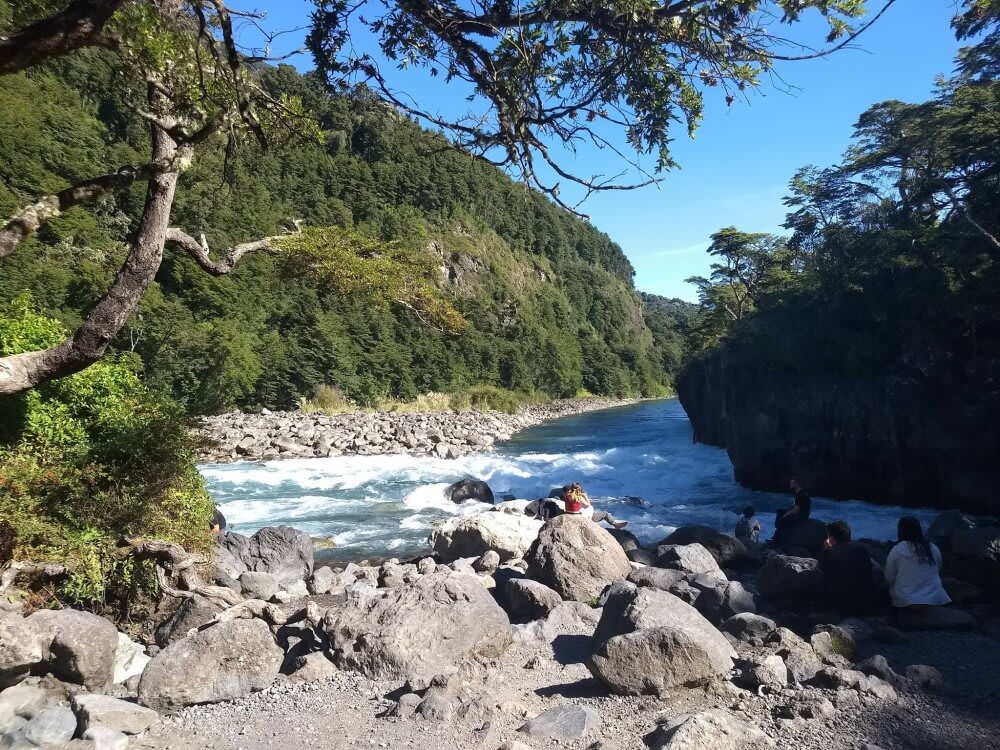 A wild river and a few people nearby sitting on rocks