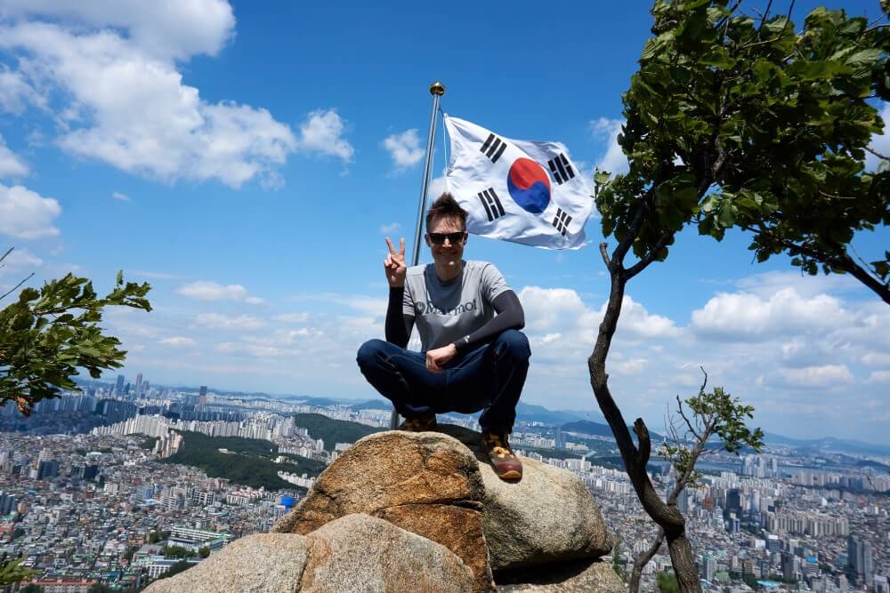 Brian sitting on a rock high up with the South Korean flag behind him 