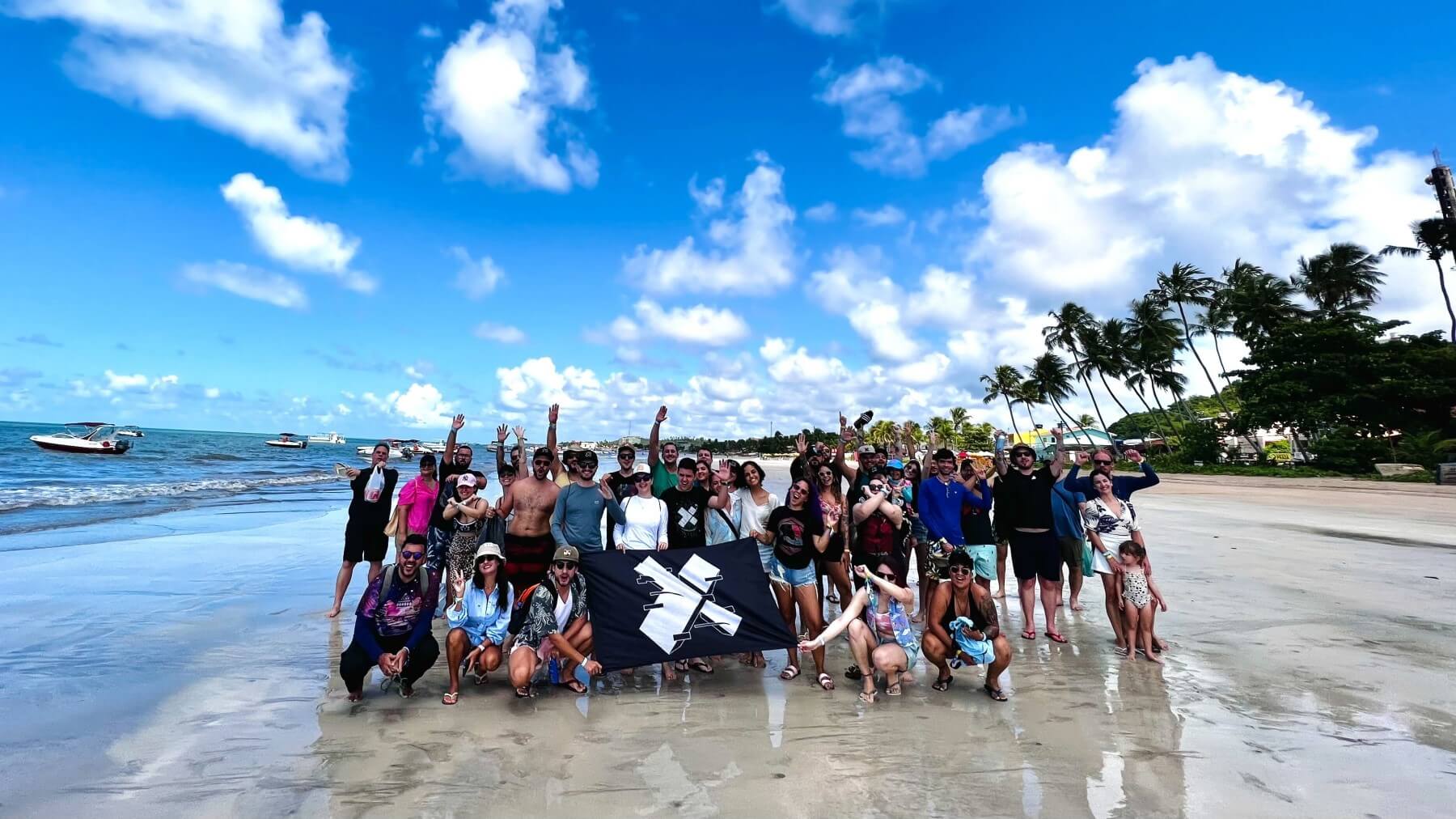 A group of X-Teamers with an X-Team flag on a sandy beach