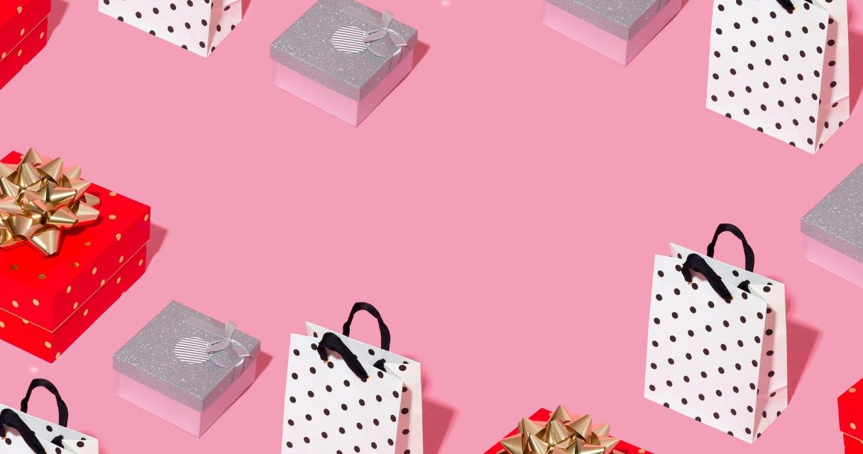 A collection of gift bags and boxes with various patterns and bows on a pink background, perfect for a festive or holiday-themed display
