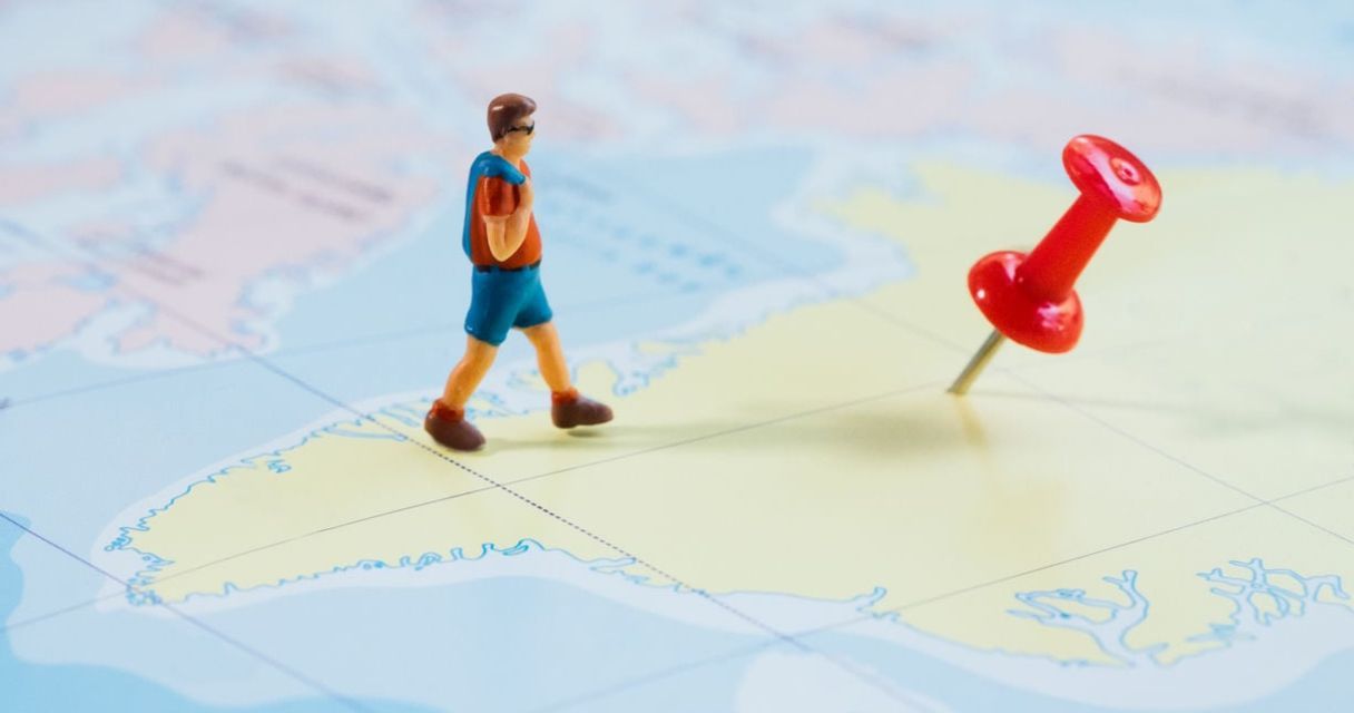  A miniature figurine of a person standing next to a red pushpin on a map, symbolizing travel, navigation, or location marking