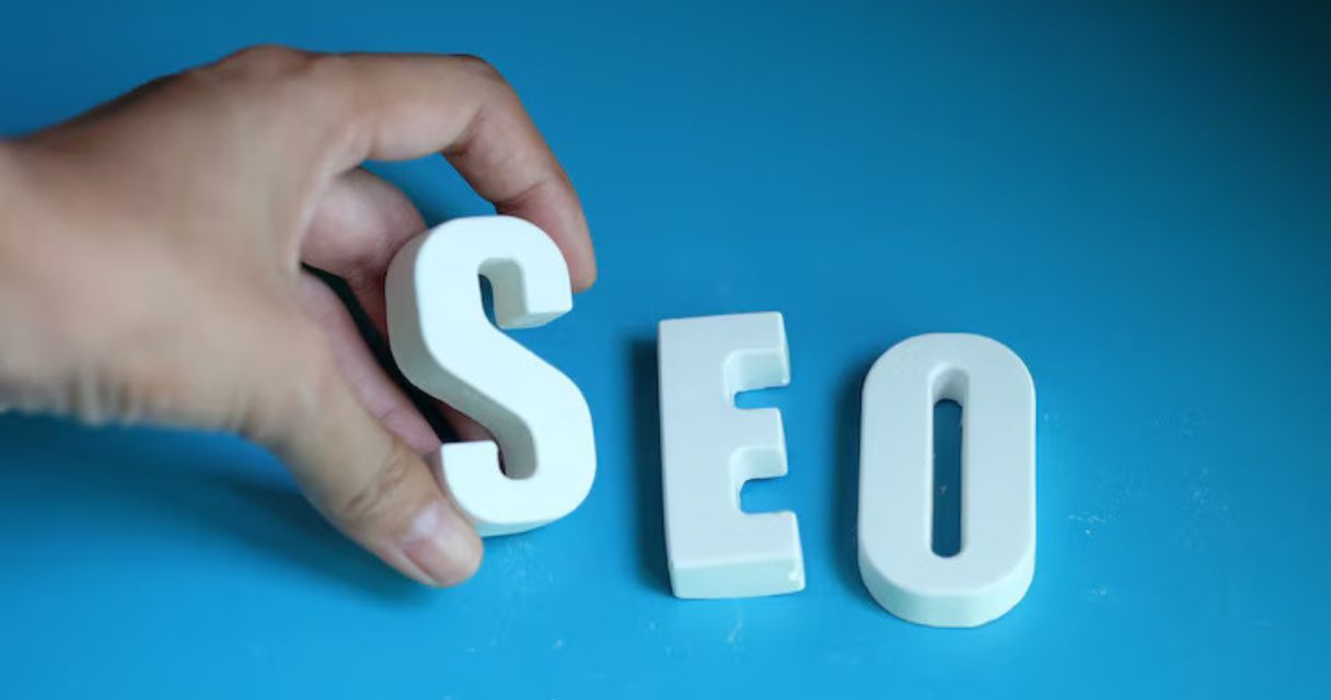 A hand arranging the letters "SEO" on a blue background, representing search engine optimization
