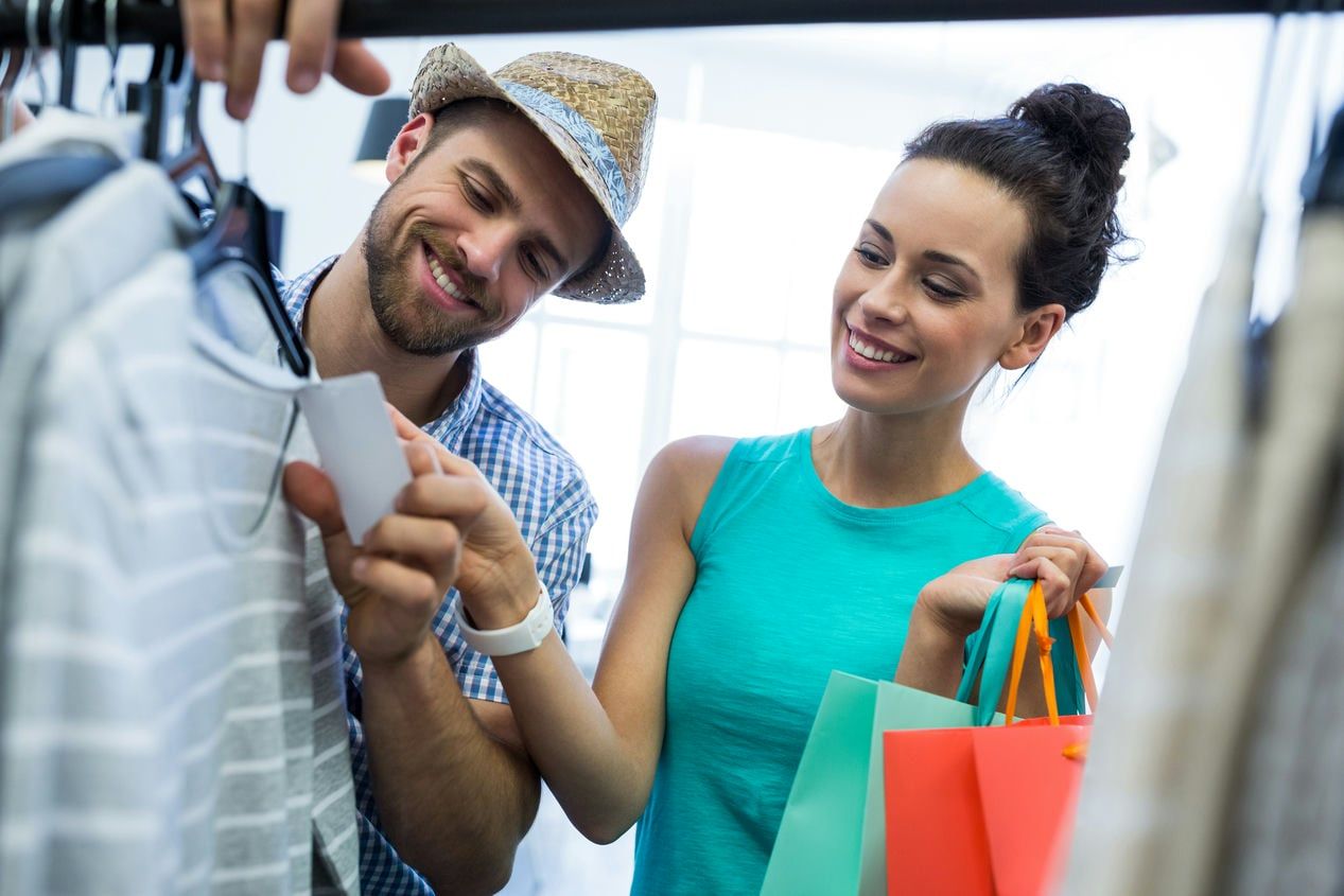 A happy couple shops together, examining a price tag on clothing, reflecting an enjoyable and engaging retail experience.