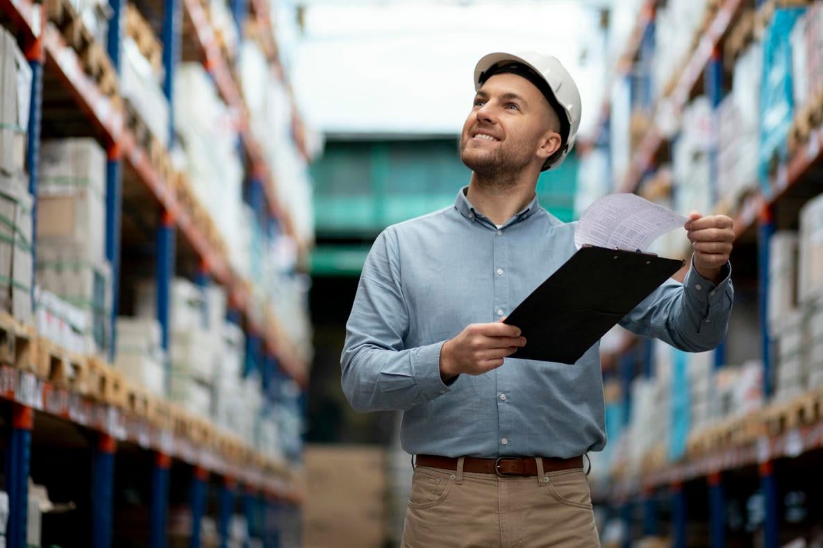 A smiling warehouse worker reviews documents on a clipboard.