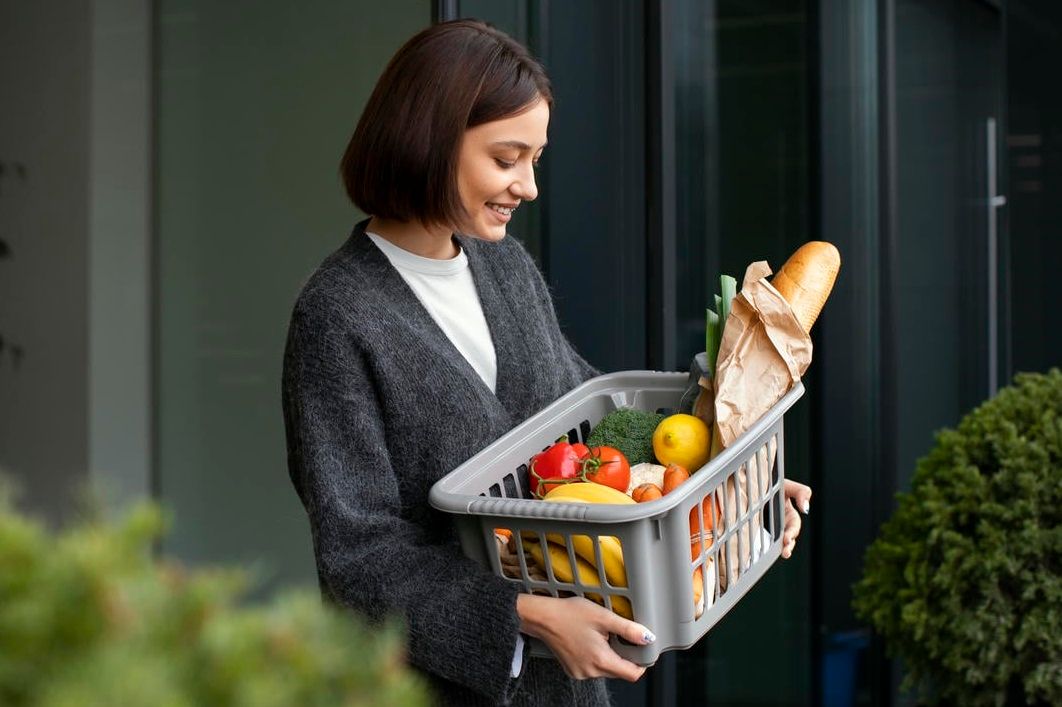 A woman smiles as she holds a basket of fresh groceries.