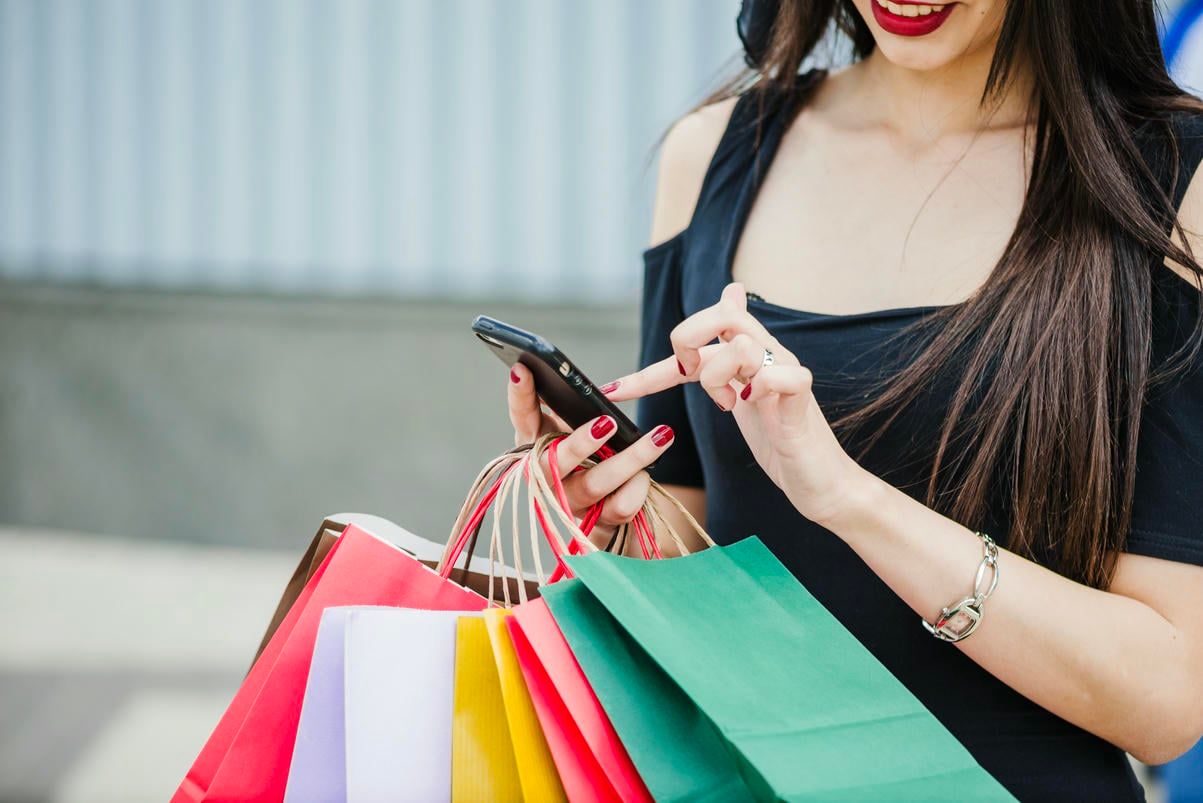 A woman uses her smartphone while holding shopping bags.