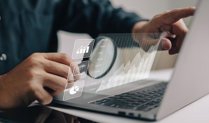 The image shows a person interacting with a laptop displaying digital graphs and charts, representing data analysis and business intelligence.