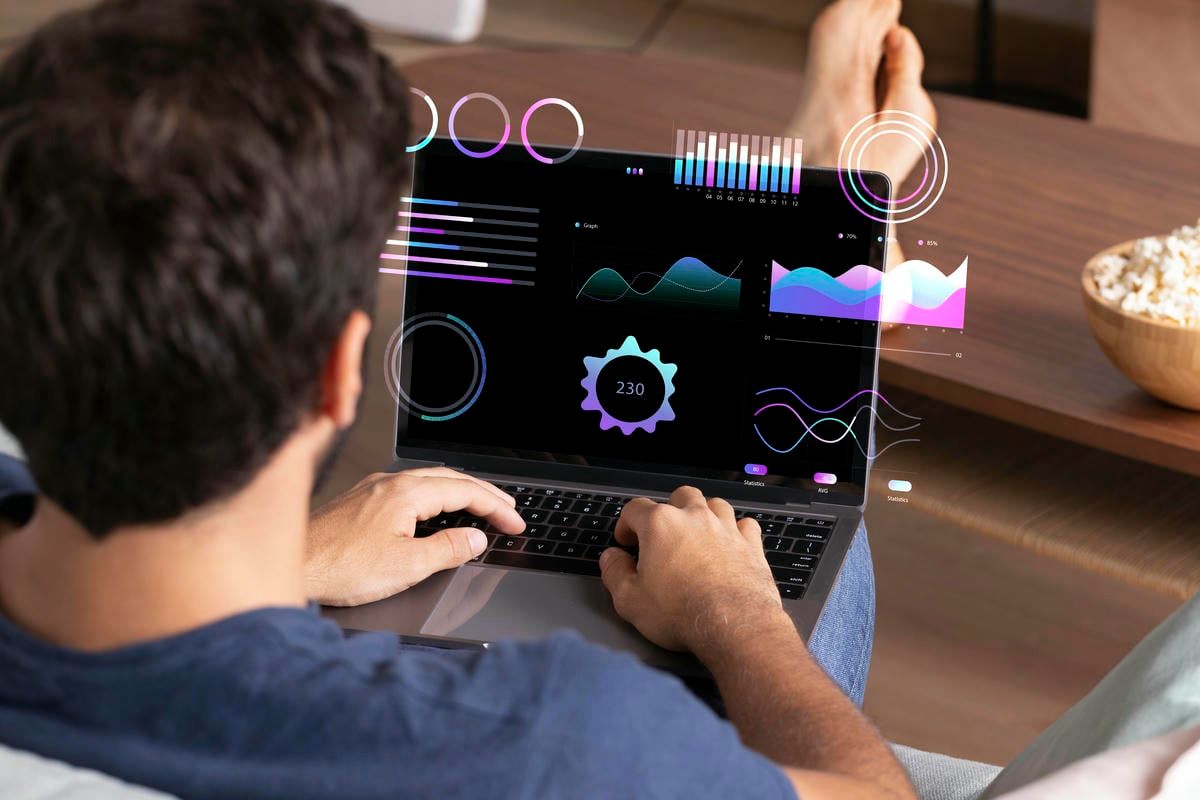 The image shows a person working on a laptop, analyzing data visualizations and graphs displayed on the screen.