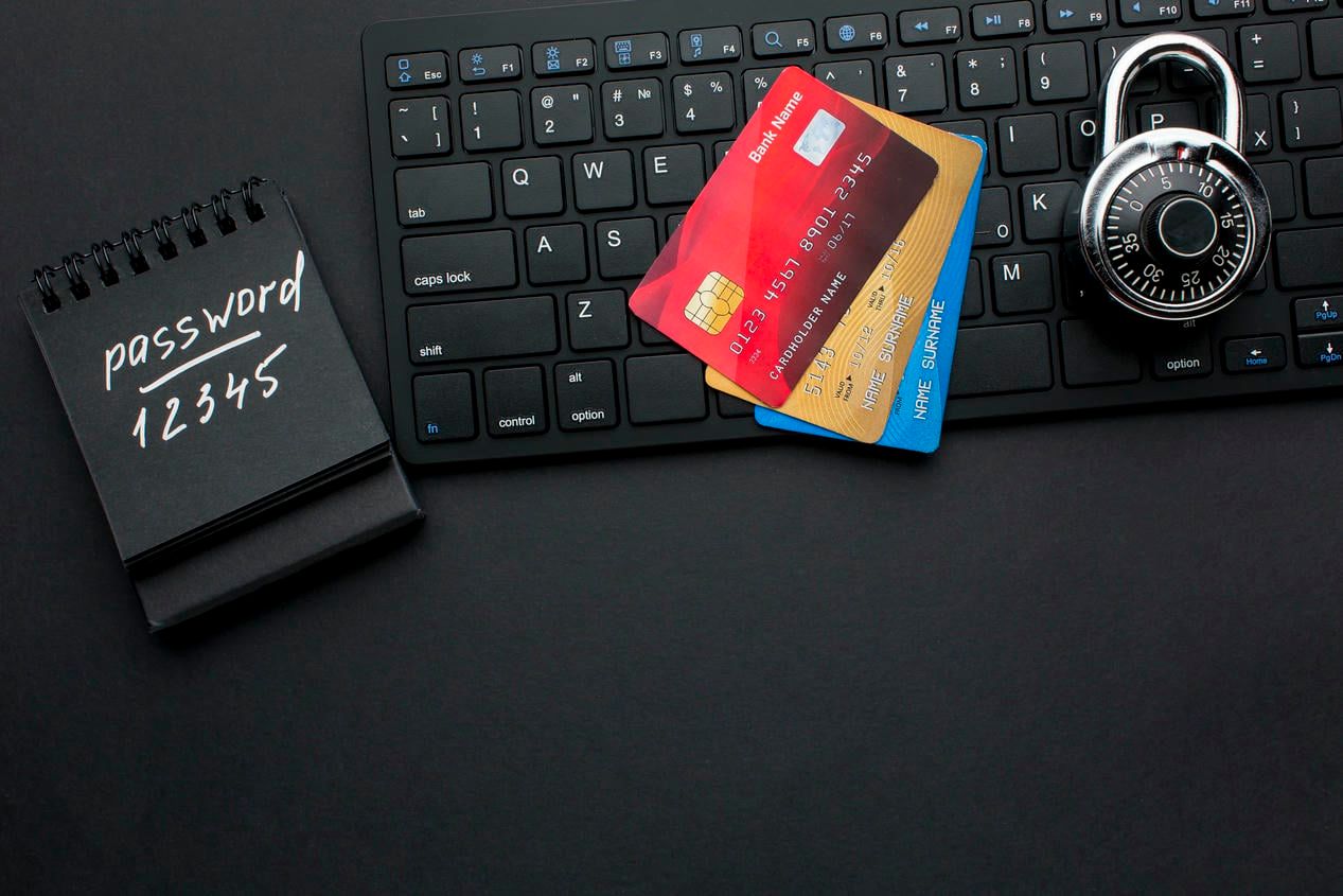 A keyboard with credit cards, a lock, and a notepad displaying a password, symbolizing the importance of securing online financial information and the risks of using easily guessable passwords.
