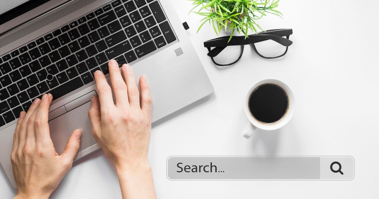 Hands typing on a laptop with a search bar overlay, symbolizing online searching.