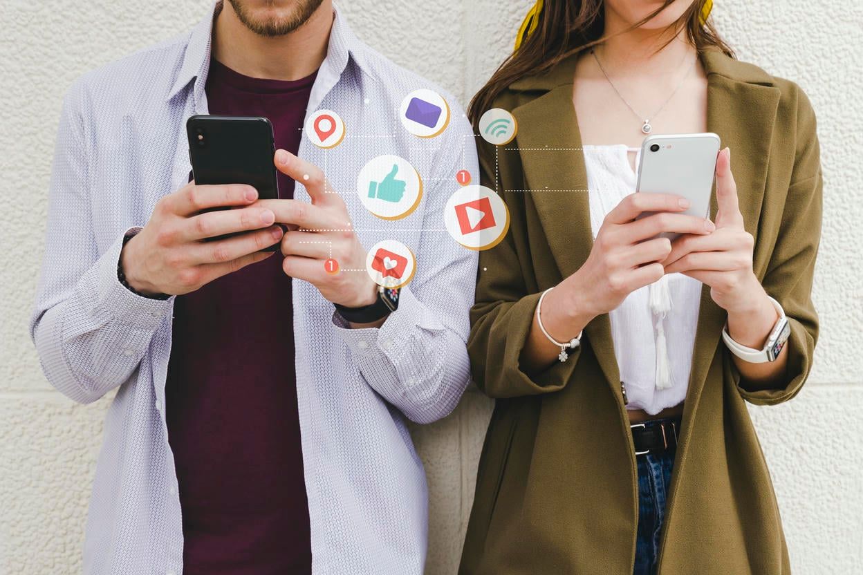 The image shows a man and a woman, each focused on their smartphones, surrounded by floating digital icons representing various social media notifications and interactions, illustrating the modern, connected lifestyle.